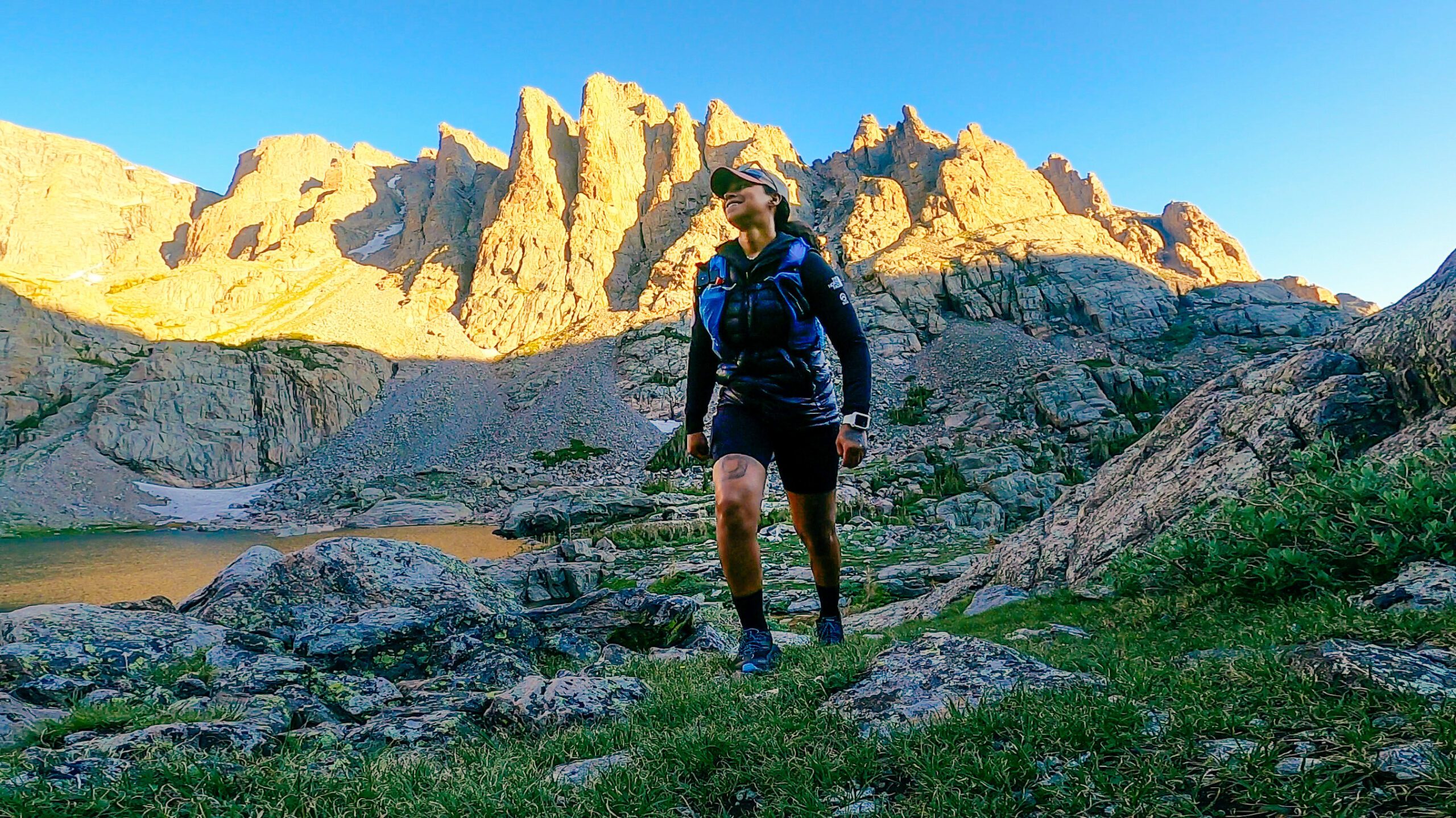 A beautiful mountain vista with a strong woman wearing a trail running vest and dressed to explore her world.